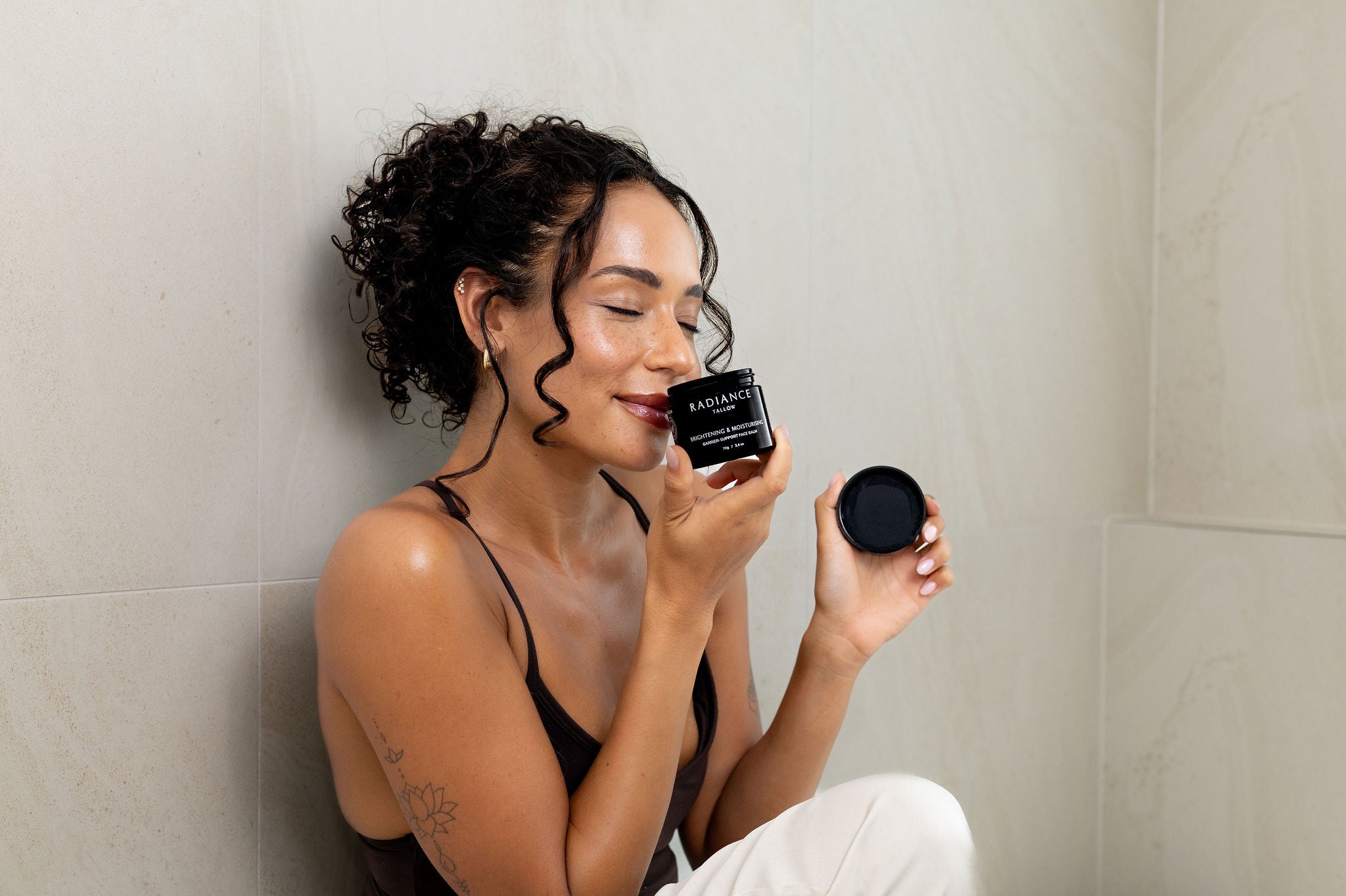 Woman holding a jar of Radiance Tallow Brightening & Moisturising Face Balm, eyes closed, inhaling the subtle citrus and chamomile scent.