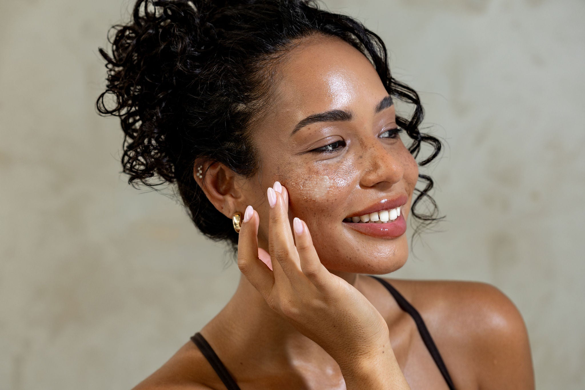 Woman with sun-kissed skin touching her face against a neutral background