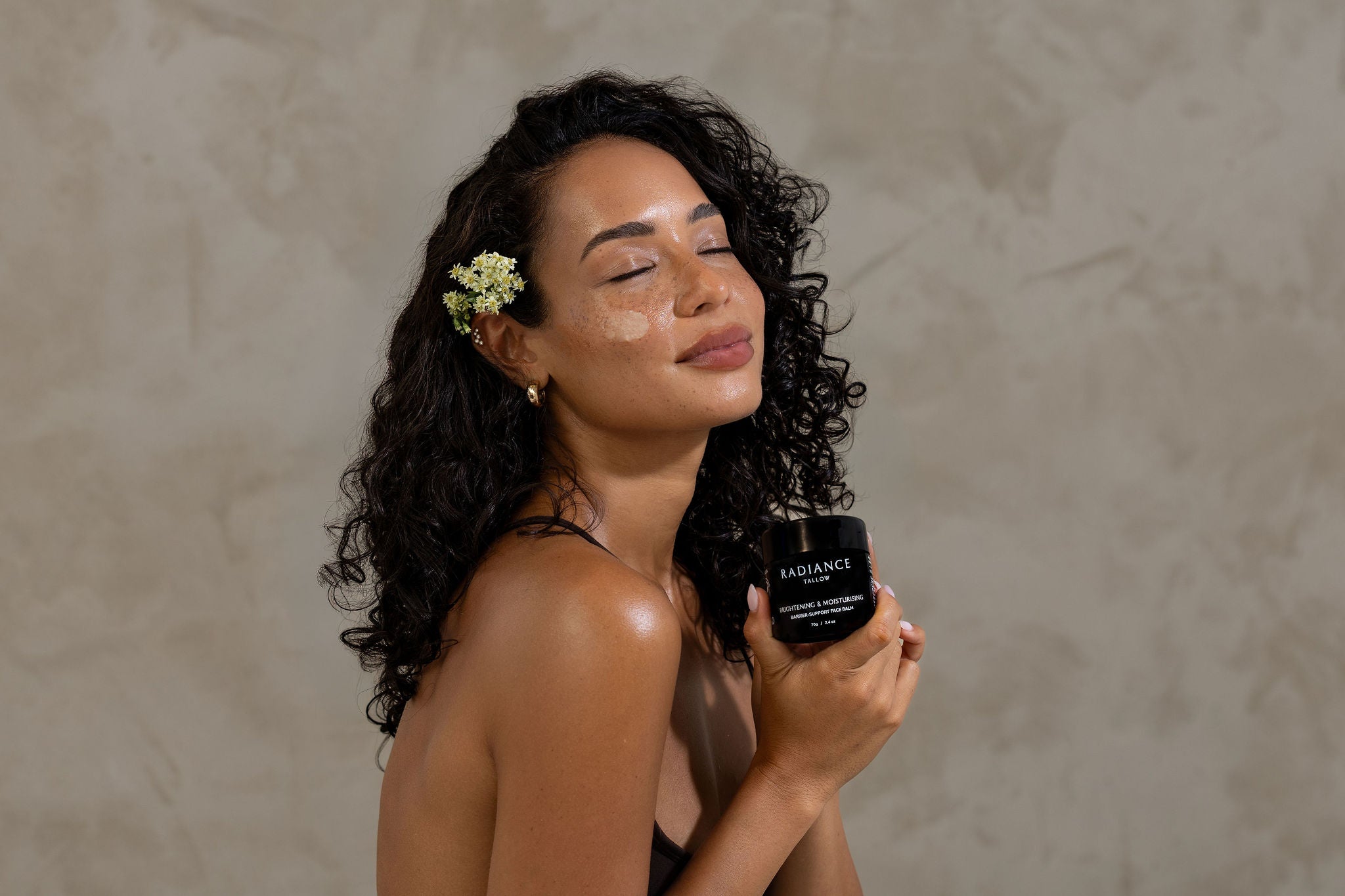 Woman holding a black bottle labeled 'Radiance Tallow' against a neutral background